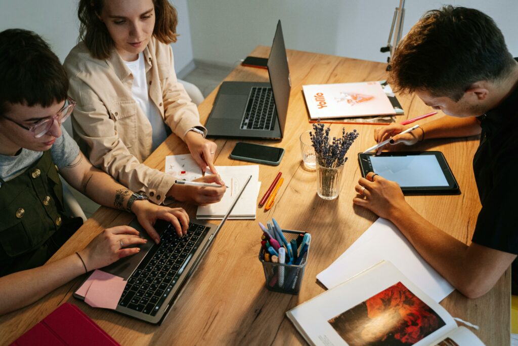Trois personnes participant à une formation sous forme d'atelier autour d'une table avec des ordinateurs portables et des documents.